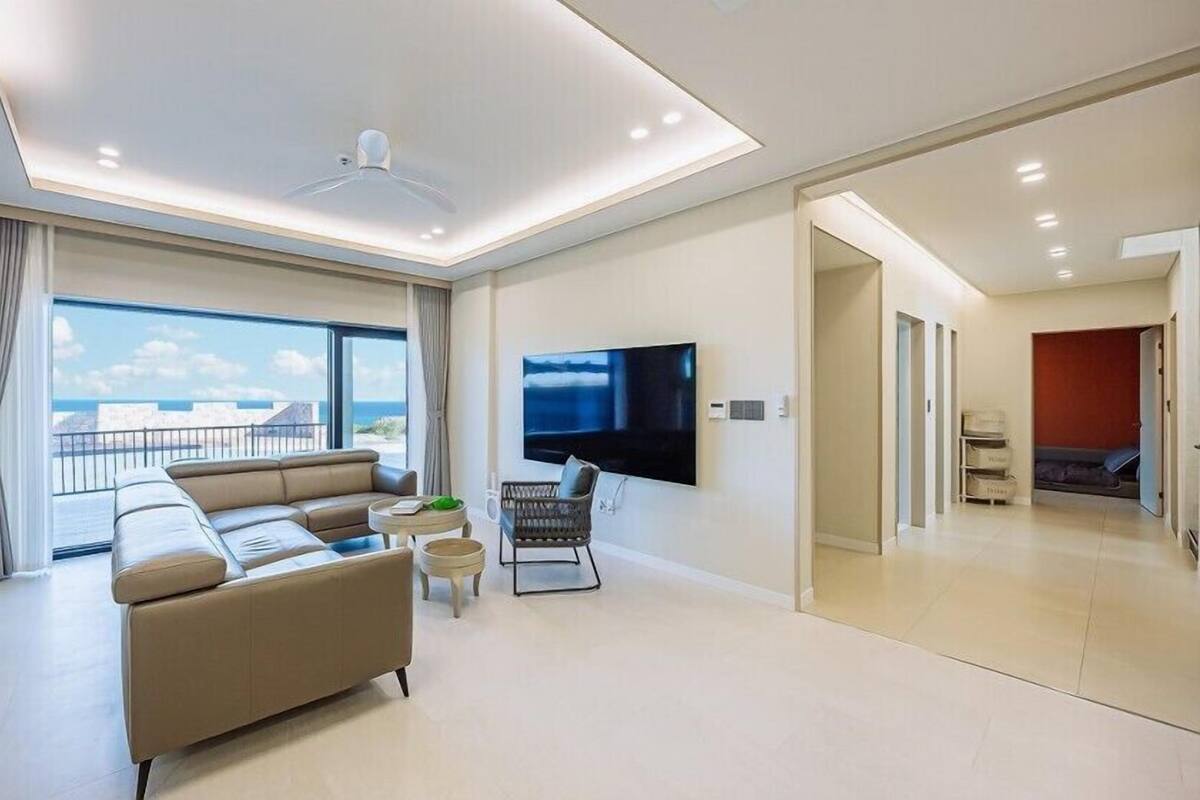 A modern living room with a sofa, a TV, and a balcony with a view.