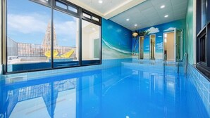 Une piscine intérieure avec des parois en verre transparent, un sol carrelé de bleu et une fresque représentant une scène de plage.