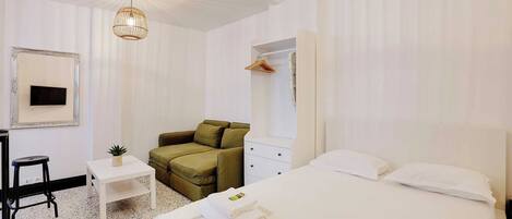 A hotel room with a bed, a desk, a chair, a small table, and a hanging light fixture.