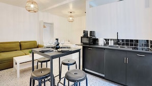 A modern kitchen with a dining area, featuring a white table set for four, a green sofa, and a black countertop with a sink and appliances.