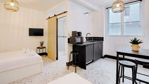 A modern hotel room with a kitchenette, a TV, a bed, and a dining area with stools.