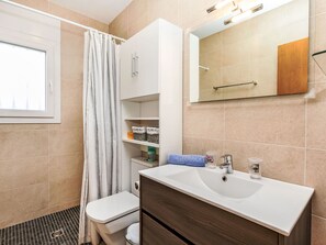 A modern bathroom with a white sink, a toilet, and a shower area. There is a mirror above the sink and a window on the left side. - Mercedes by Interhome (Sant Jaume dels Domenys)