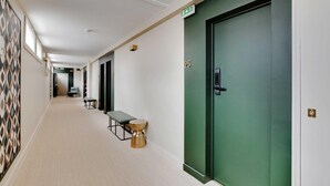 A hotel hallway with a green door marked "25", a bench, a small table, and a patterned wall. - Modern "Green Suites" residence - Meudon/Vélizy (Meudon)