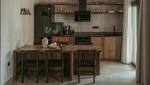 A modern kitchen with wooden cabinets, a central island, and a dining area with four chairs. - Pure Beachfront Villa with pool (Sithonia)