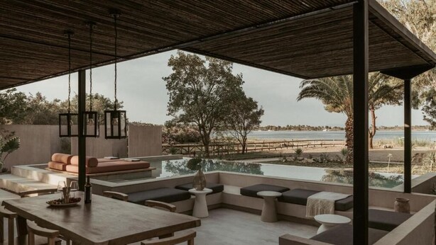 An outdoor seating area with a pool, wooden furniture, and a view of the beach. - Pure Beachfront Villa with pool (Sithonia)