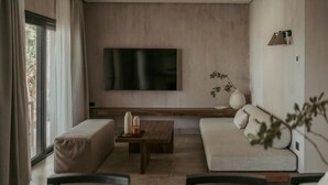 A modern living room with a large flat-screen TV mounted on the wall, a sofa, a bench, and a coffee table. - Pure Beachfront Villa with pool (Sithonia)