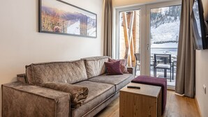A modern living room with a sofa, a small wooden table, and a TV. - Cosy apartment with view (Rauris)
