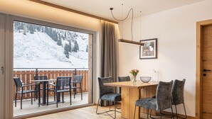 Quarto com mesa e cadeiras de madeira, uma grande janela com vista para uma montanha nevada e uma porta de madeira.