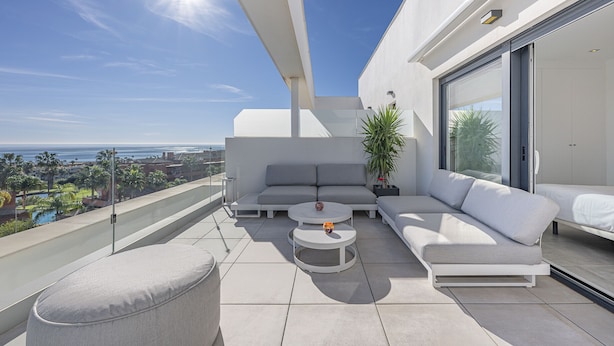 A modern balcony with a sofa, two round tables, and a potted plant.