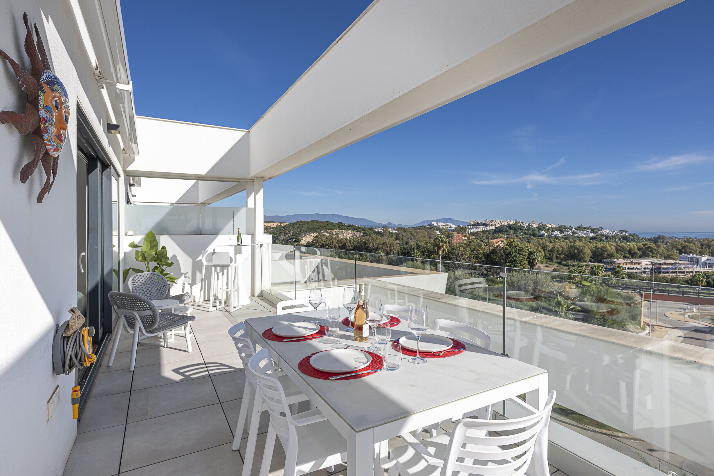 Un balcón con una mesa blanca dispuesta para comer, sillas blancas y una vista despejada del paisaje.