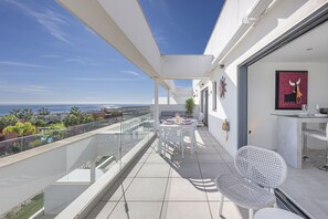 A balcony with a glass railing, a dining table with chairs, and a view of the sea. - Luxury Penthouse with Seaview & Golf 5010 (Casares)