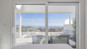 A modern bedroom with a large sliding glass door leading to a balcony with a city view.