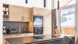Eine moderne Küche mit Holzausstattung, integriertem Backofen und einem großen Fenster mit Blick auf eine verschneite Landschaft.