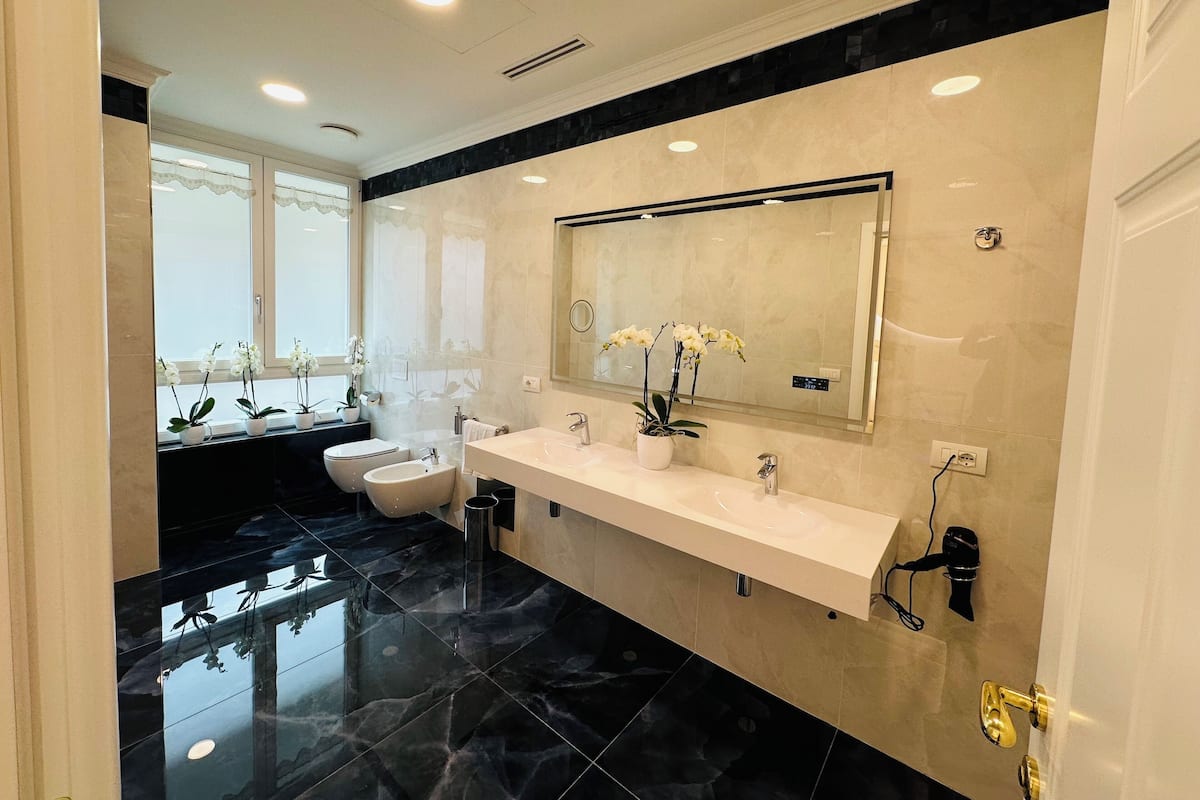 A modern bathroom with a large mirror, two sinks, a toilet, and potted orchids.