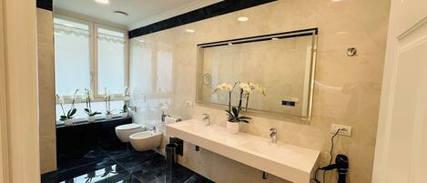 A modern bathroom with a large mirror, two sinks, a toilet, and potted orchids.