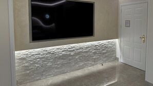Un corridoio moderno con un grande televisore a schermo piatto montato su una parete strutturata, una porta bianca con maniglia in ottone e una parete di pietra ruvida alla base.
