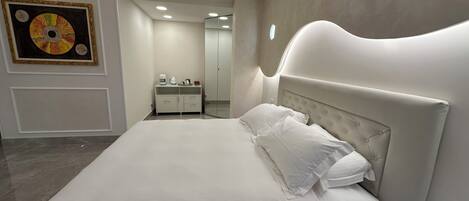 A modern bedroom with a large bed, a bedside table, a nightstand, a wardrobe, and a mirror.