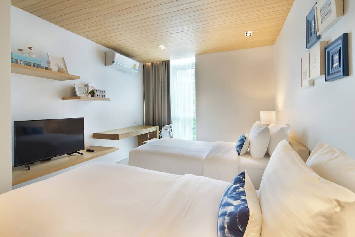 A hotel room with two beds, a TV, a desk, and shelves with decorative items.