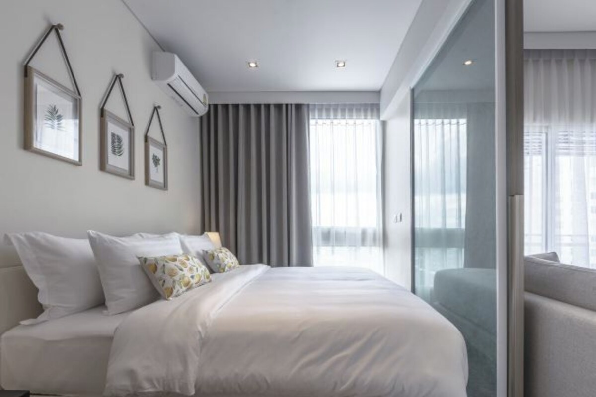 A modern hotel room with a large bed, a sofa, and a glass partition.
