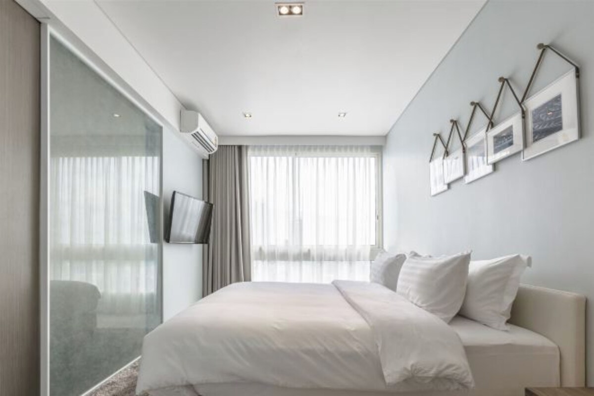 A modern hotel room with a large bed, a flat-screen TV, and a large window with curtains.