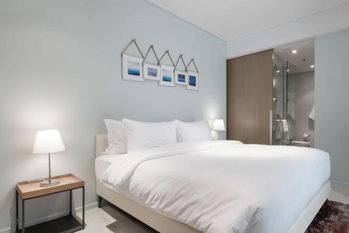 Habitación de hotel con una cama grande, lámparas de noche, una mesita de noche y un cuadro colgado en la pared.