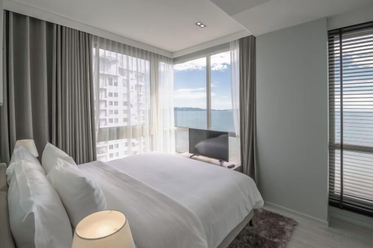 A modern bedroom with a large bed, a TV, and a view of the sea.