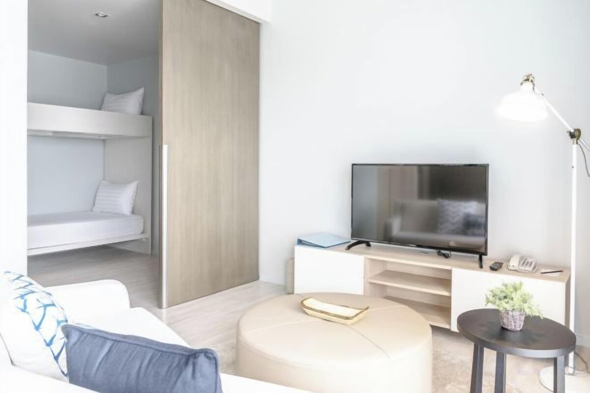 A modern hotel room with a bed, TV, sofa, and a small table with a plant.