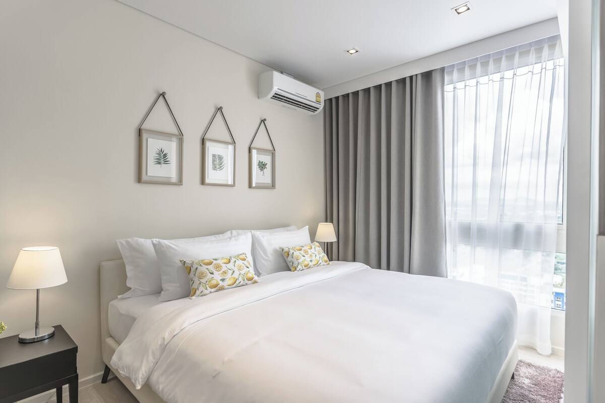 A hotel room with a large bed, two bedside lamps, a nightstand, and a window with curtains.
