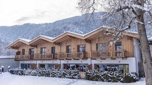 A wooden chalet with multiple balconies and large windows, surrounded by snow-covered trees and mountains. - Nice apartment with balcony (Reith bei Kitzbühel)