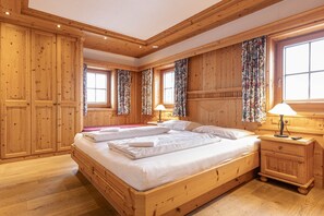 A wooden room with a large bed, two windows with floral curtains, and wooden cabinets. - Nice apartment with balcony (Reith bei Kitzbühel)