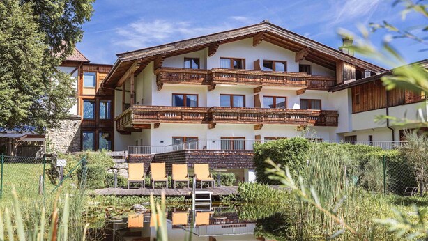 A multi-story hotel with wooden balconies and a reflection in the water. - Nice apartment with balcony (Reith bei Kitzbühel)