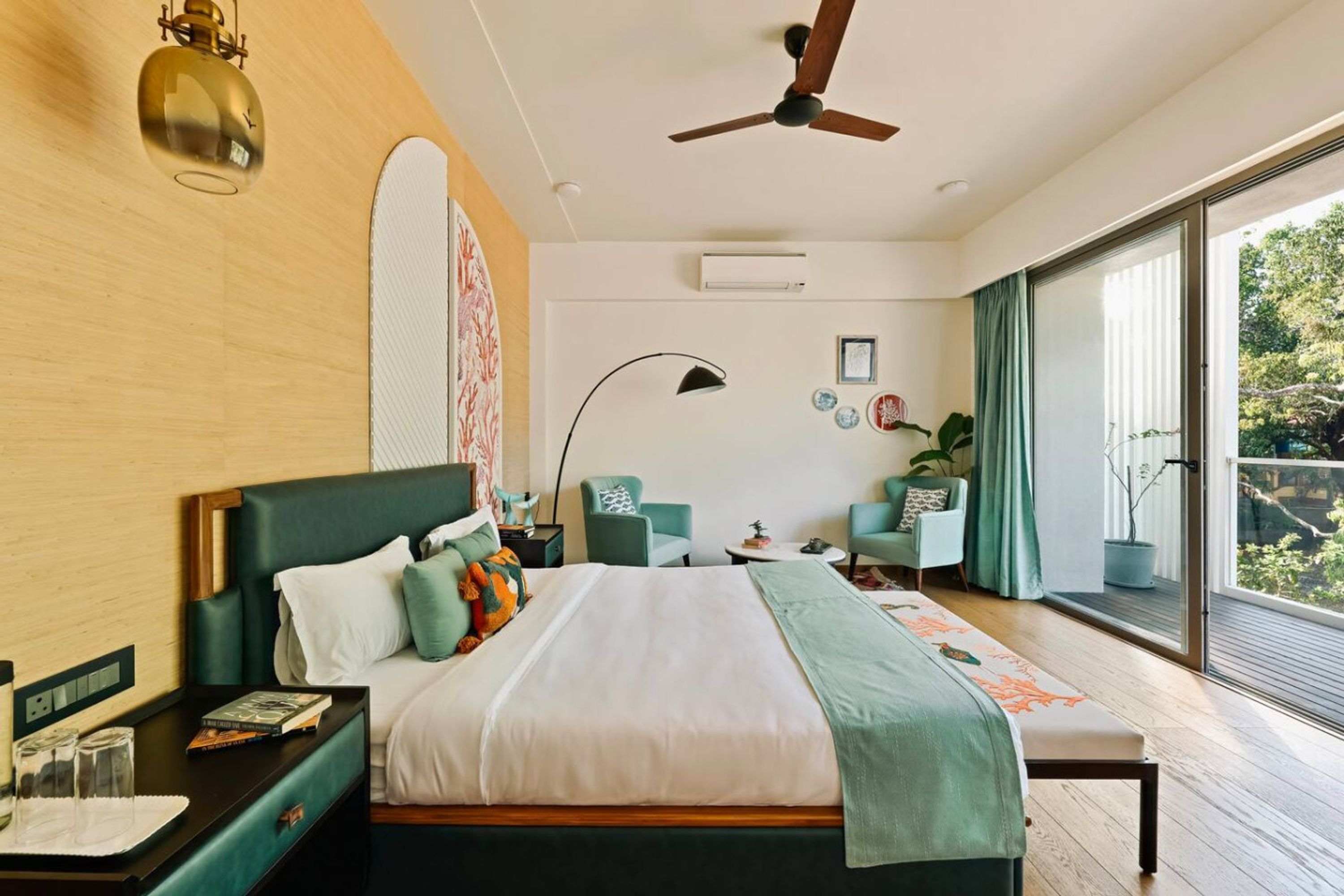 A modern bedroom with a large bed, a ceiling fan, a bedside table with glasses, a nightstand, and a view of the outdoors through a sliding glass door.