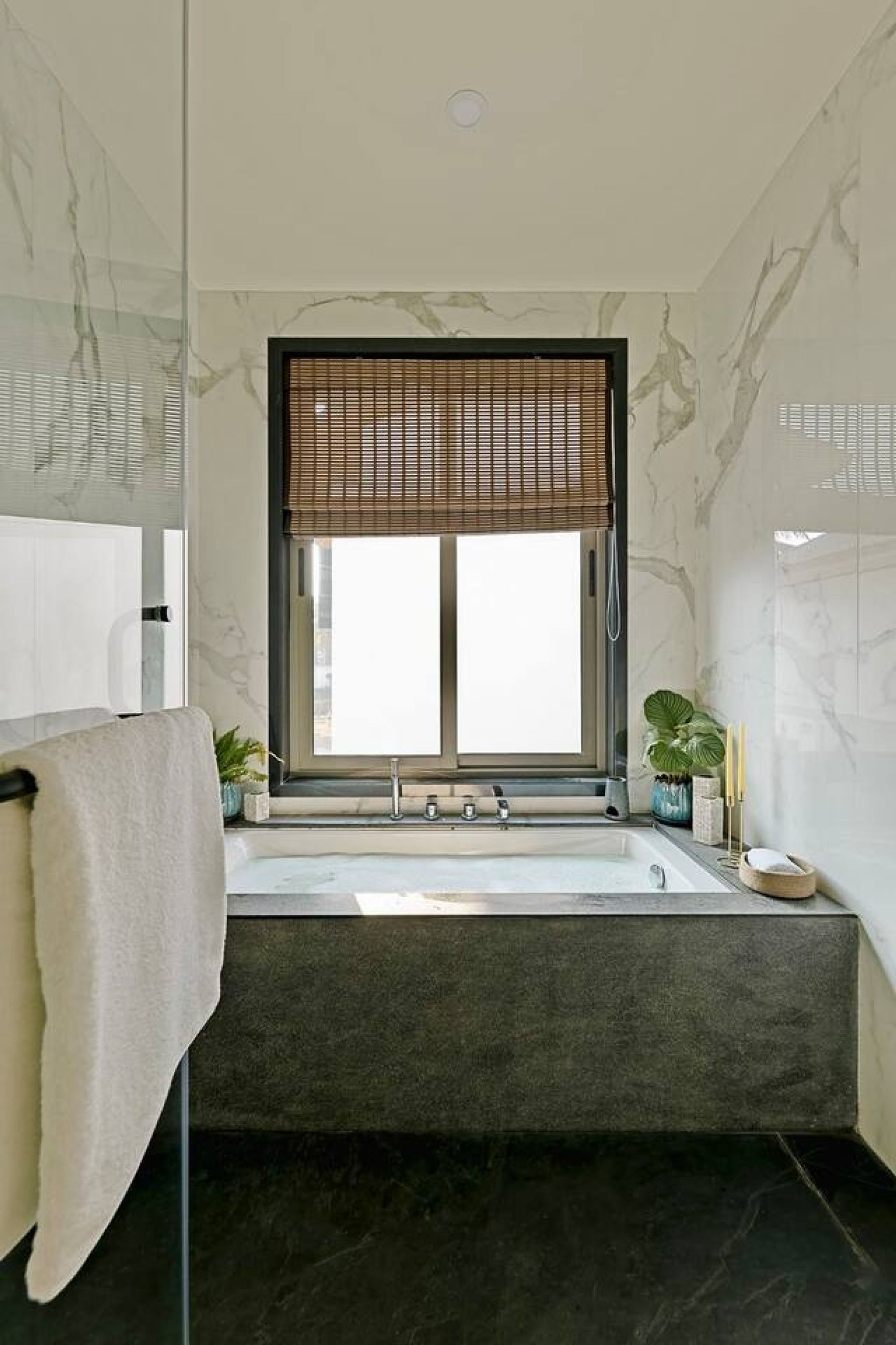 A modern bathroom with a freestanding bathtub, a window with a bamboo blind, and a towel rack.