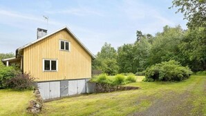 A yellow wooden house with a single window and a chimney, surrounded by a grassy yard and dense trees. - Oas Finnerödja (Finnerödja)