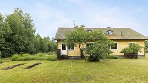 A single-story house with a sloped roof, a front porch, and a small garden area with a tree and shrubs. - Oas Finnerödja (Finnerödja)