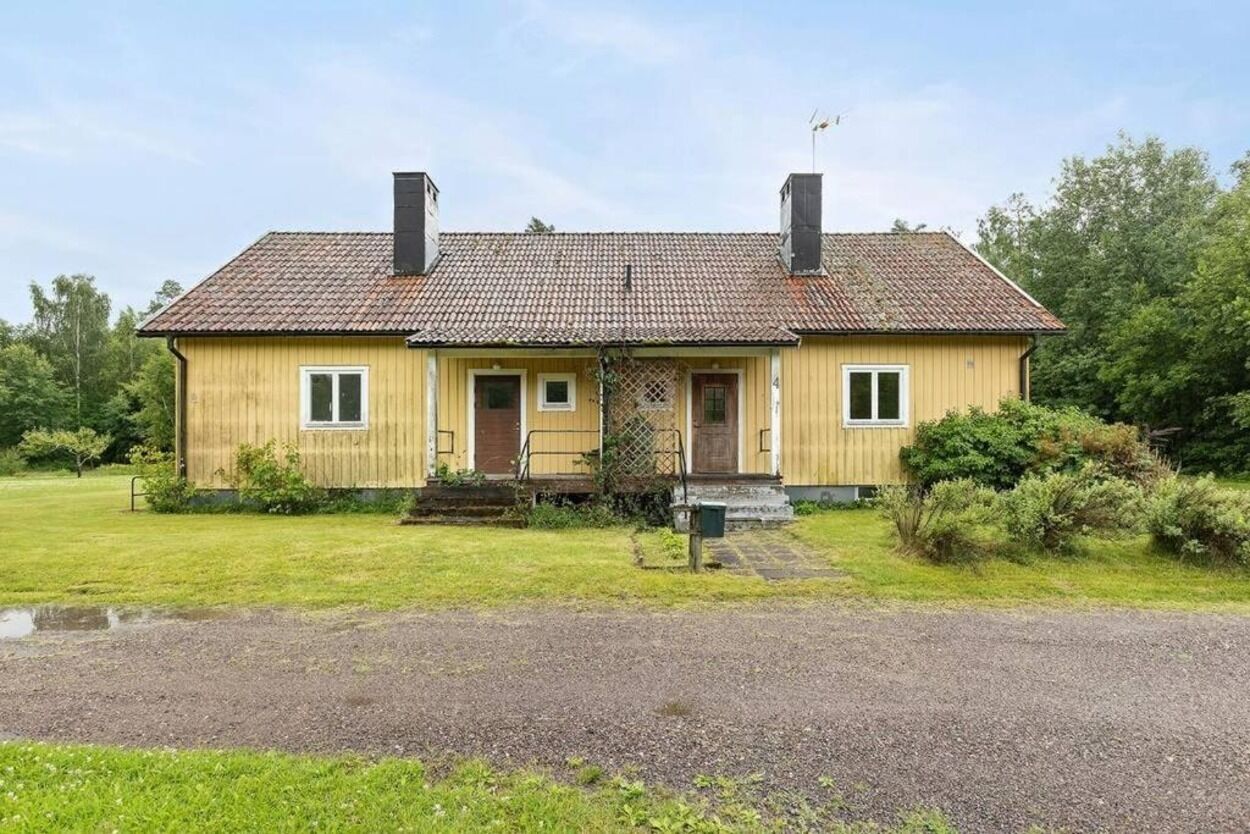 A two-story wooden house with a tiled roof, a front porch, and a small garden area.
