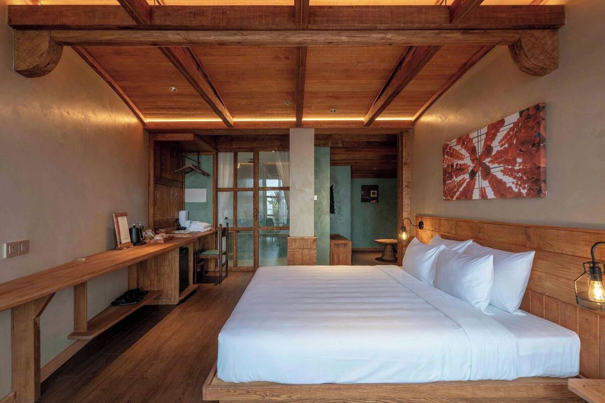 Une chambre à coucher avec un grand lit, une tête de lit en bois, un banc avec une table et un luminaire fixé au mur.