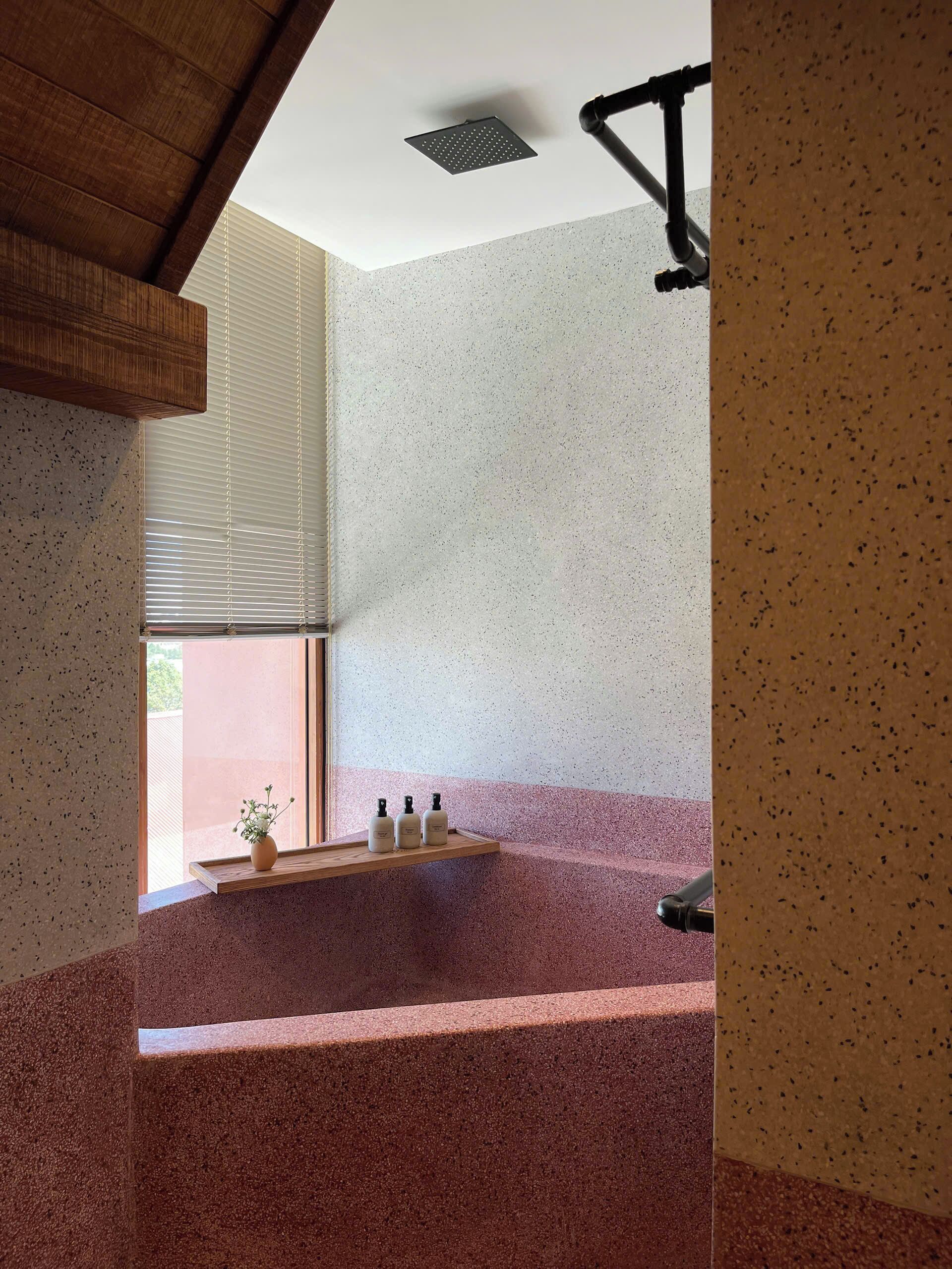 Une salle de bain moderne avec un carrelage à motifs, une étagère en bois où sont rangés les articles de toilette et une fenêtre avec des stores.