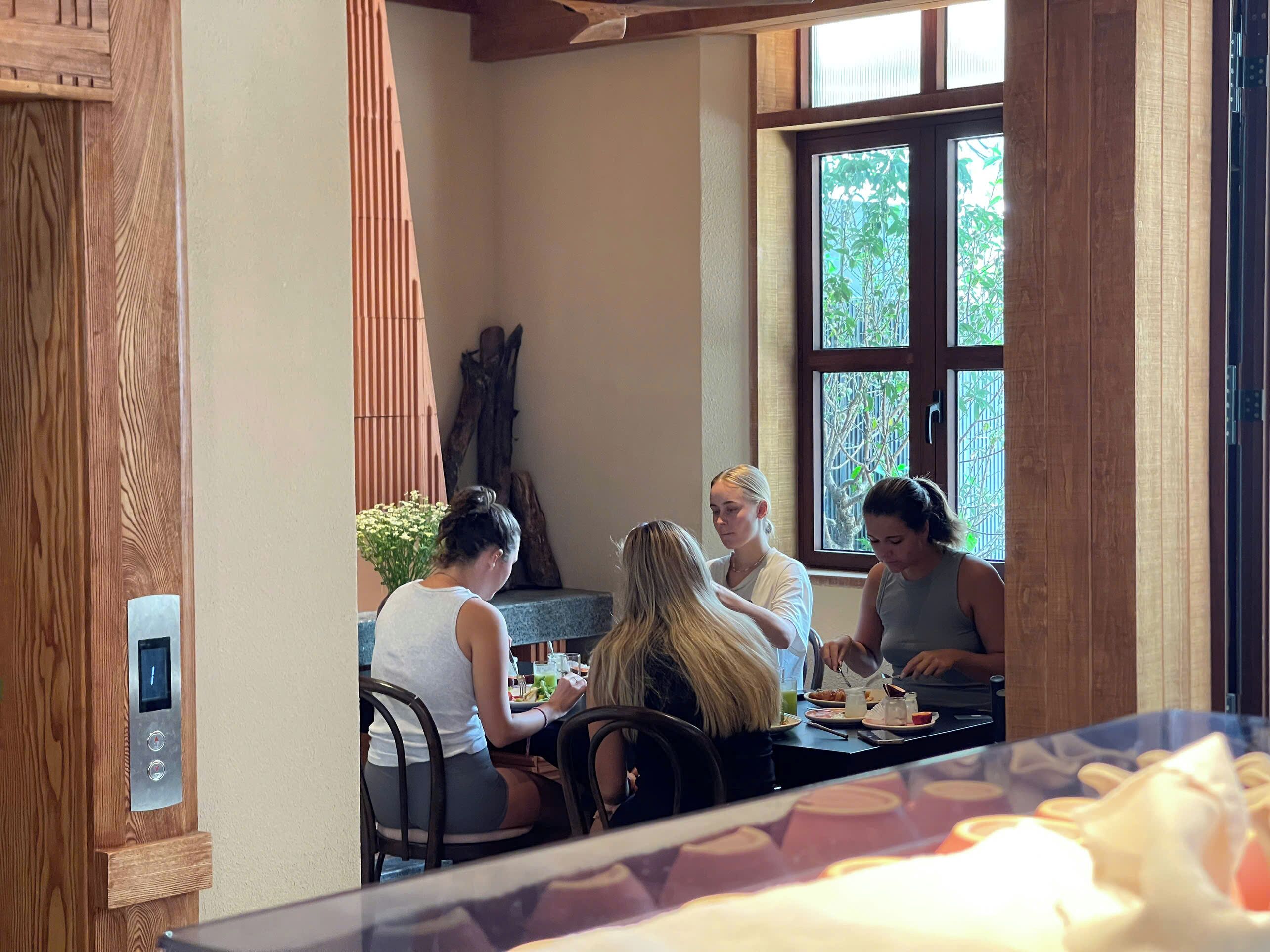 A group of people dining at a table with a view of greenery outside.