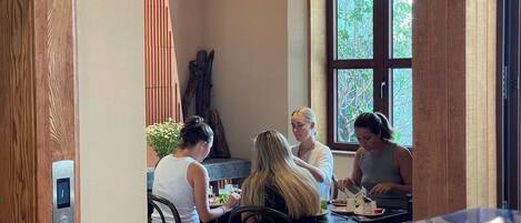A group of people dining at a table with a view of greenery outside.
