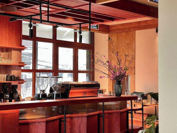 A bar area with wooden furniture, a coffee machine, and a vase with flowers.