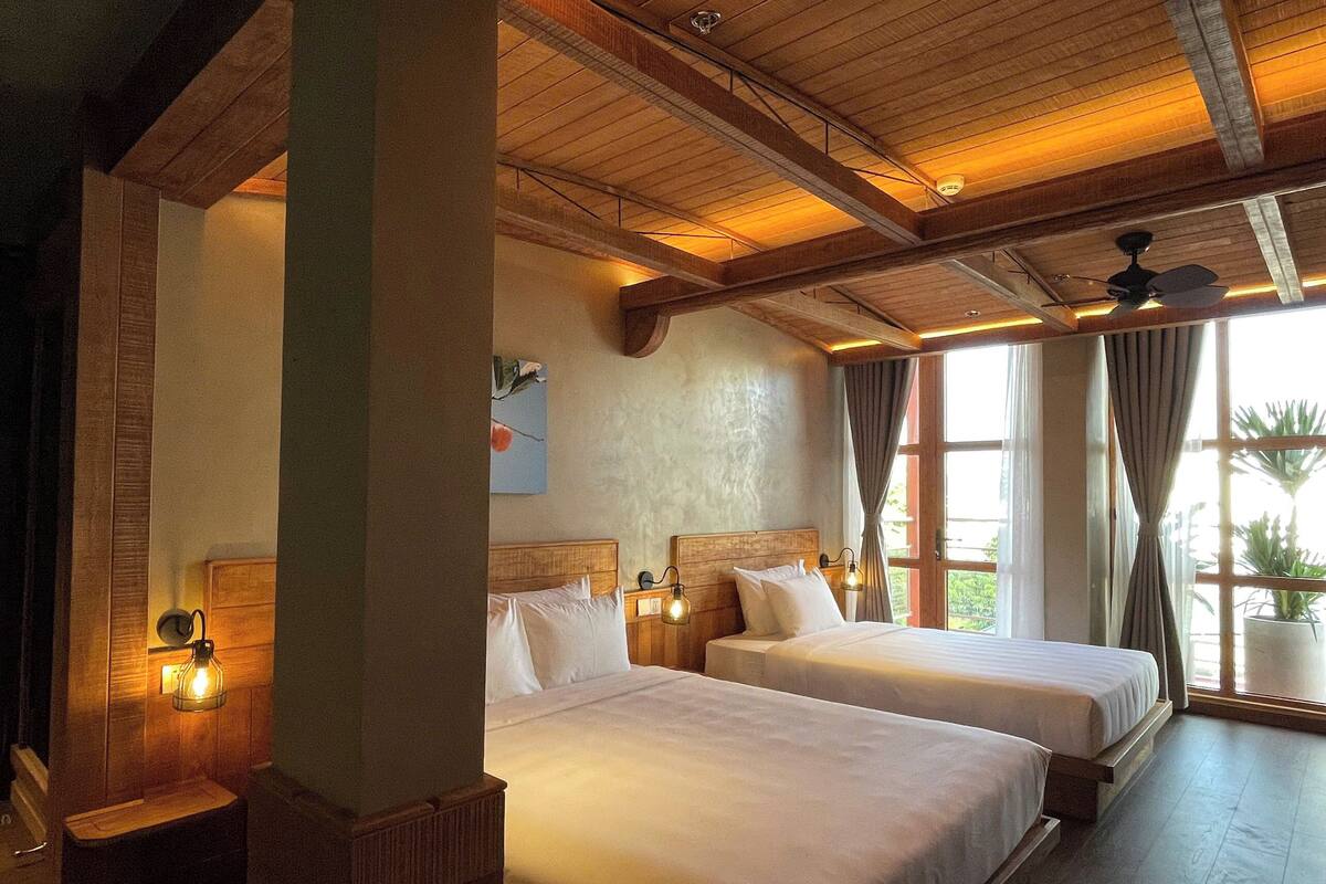 Une chambre d’hôtel avec deux lits, des poutres en bois au plafond et une grande fenêtre avec des rideaux.