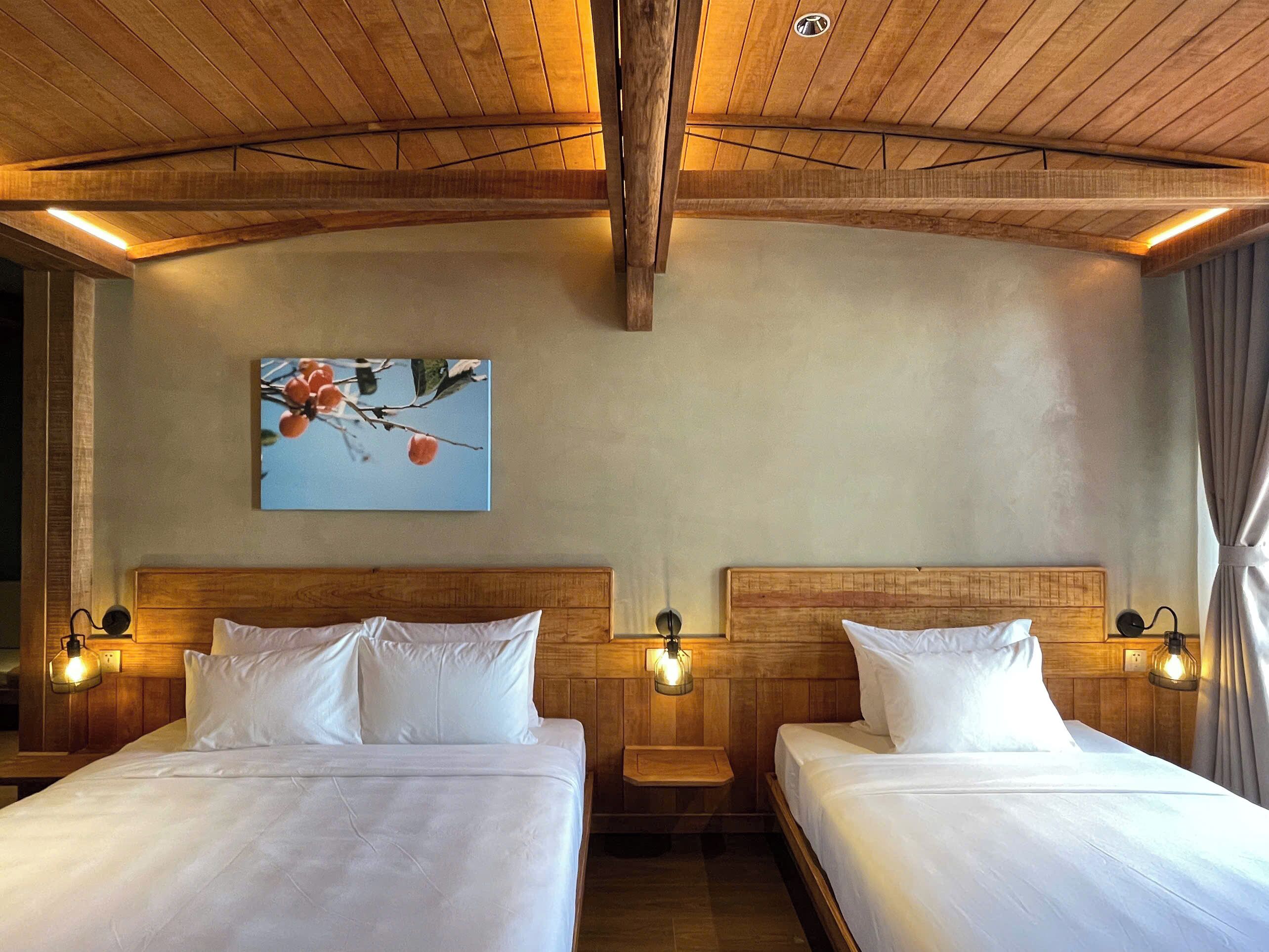 A hotel room with two beds, wooden headboards, and wall-mounted lamps.