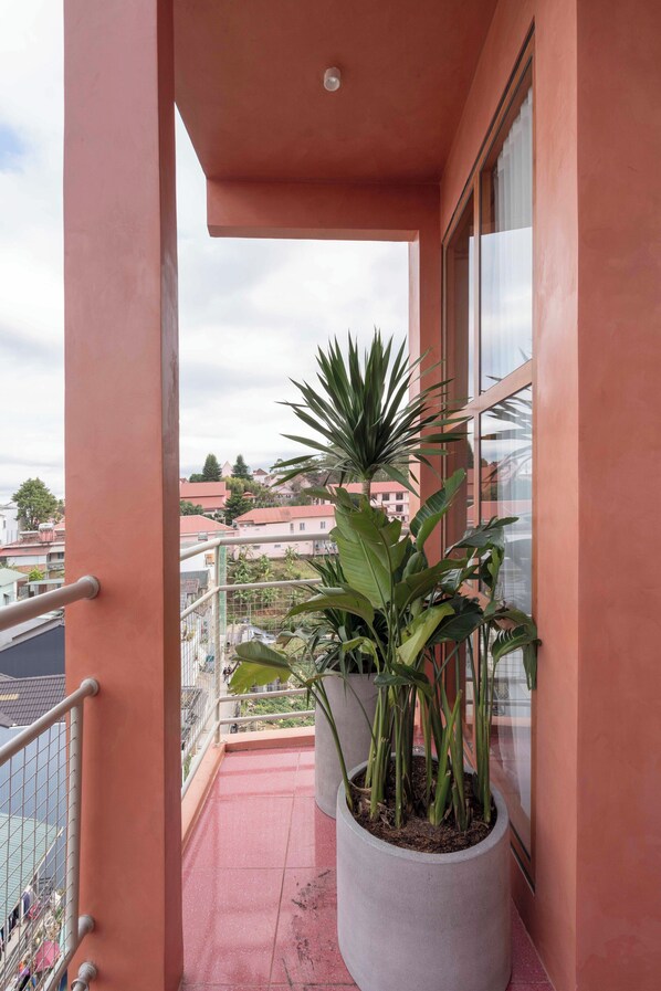 Un balcon avec un pot de fleurs, une balustrade et une vue sur des bâtiments en arrière-plan.