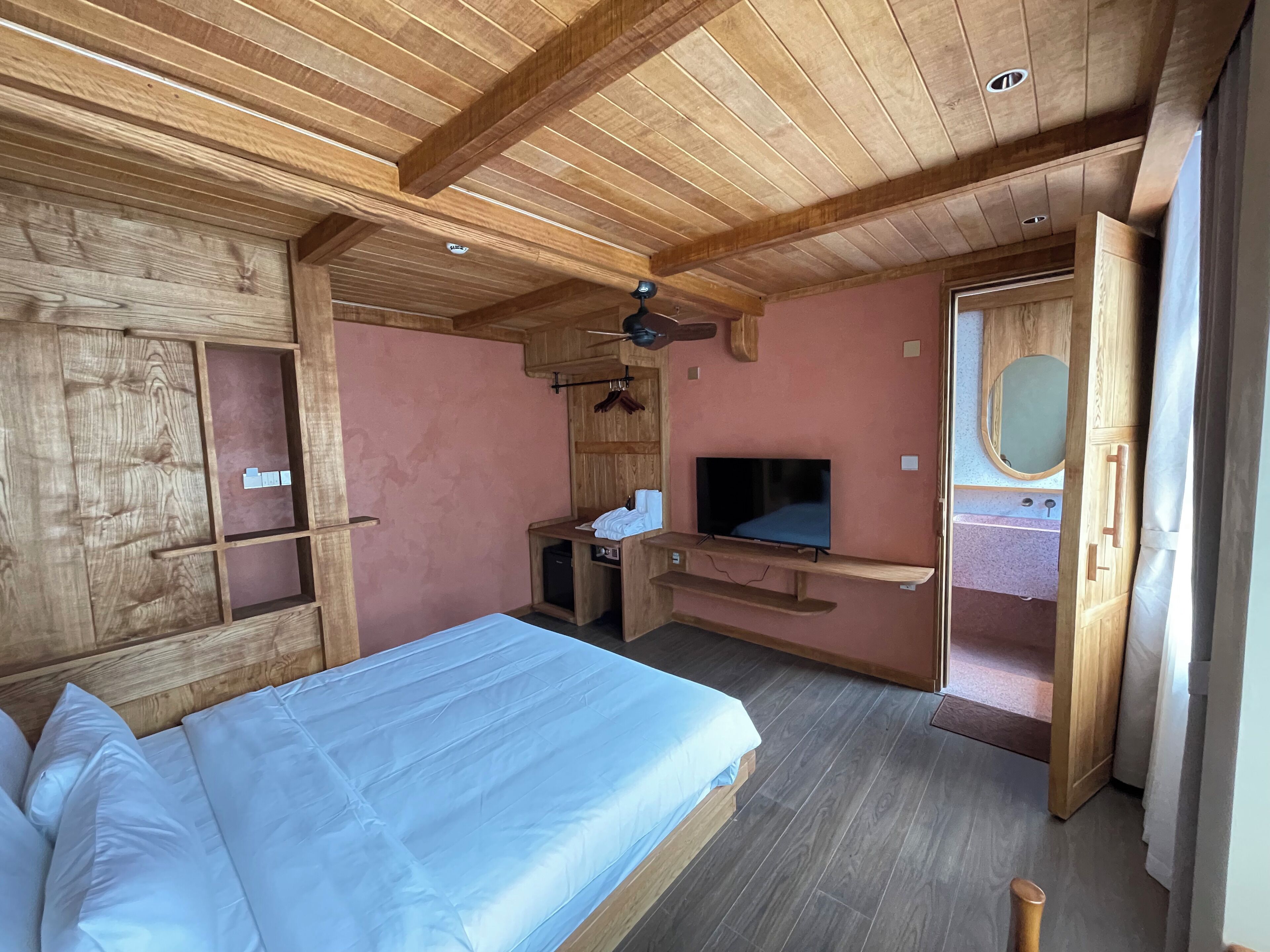 Ein Schlafzimmer aus Holz mit einem Bett, einem Fernseher, einem kleinen Schreibtisch und einem Badezimmer.