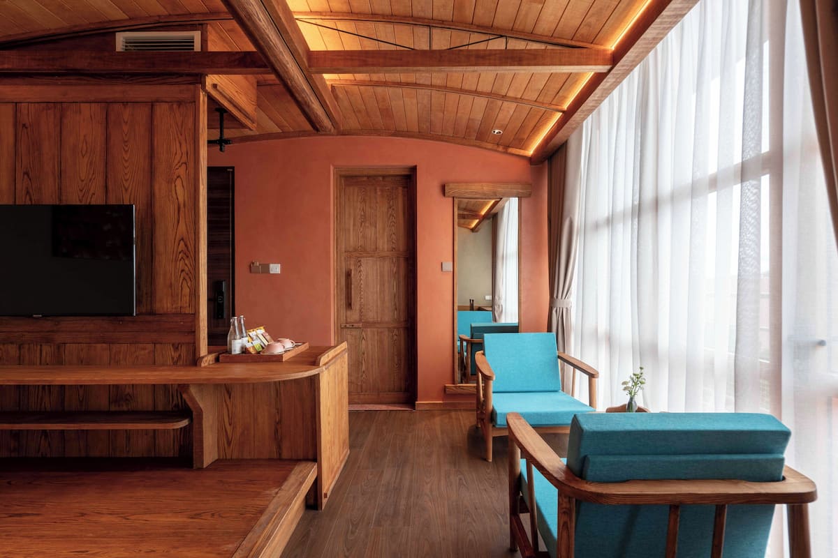 Un salon chaleureux, doté de meubles en bois, d’un téléviseur à écran plat et d’une grande fenêtre ornée de rideaux légers.