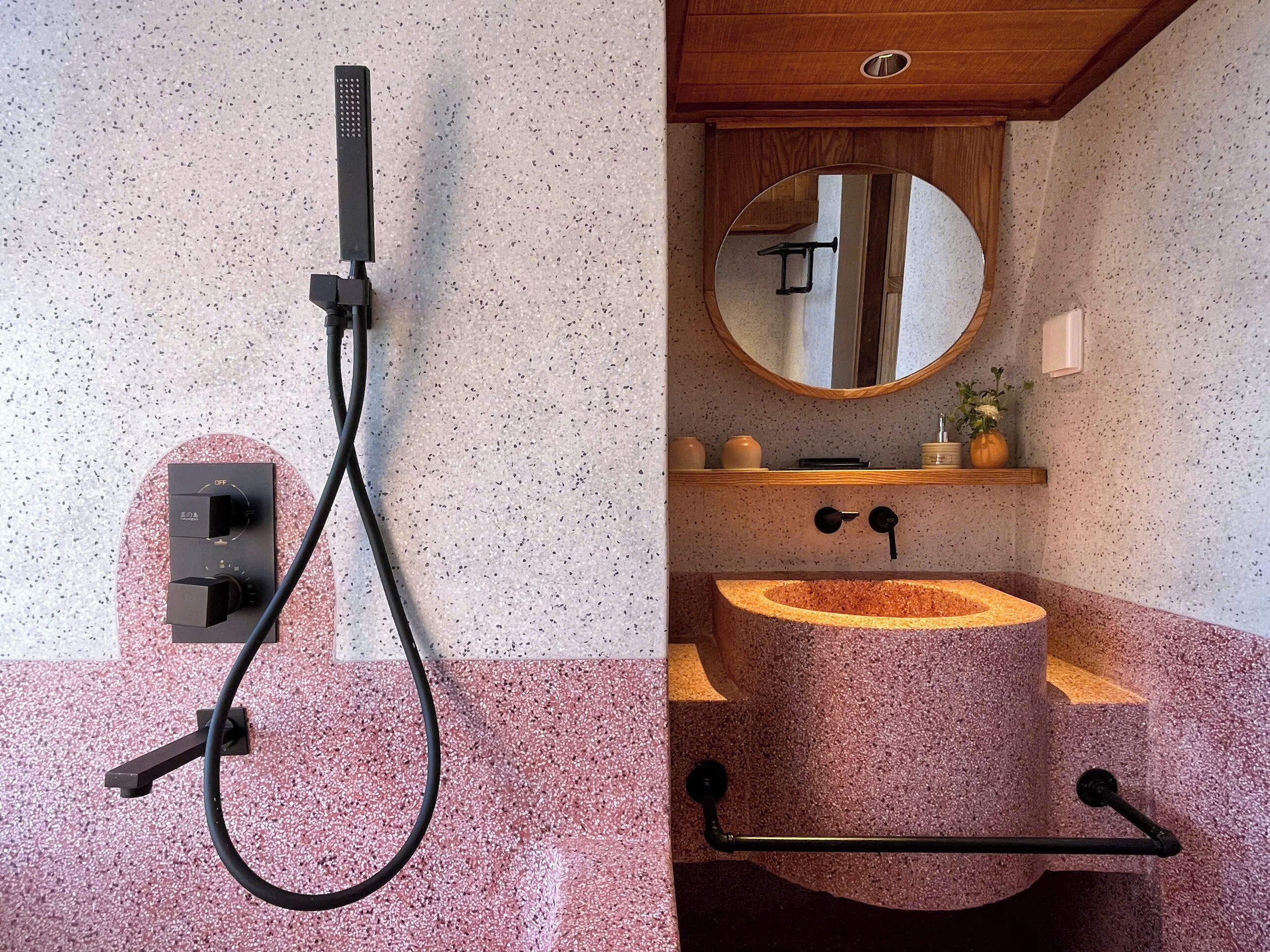 A bathroom with a freestanding shower, a round mirror, and a granite sink.
