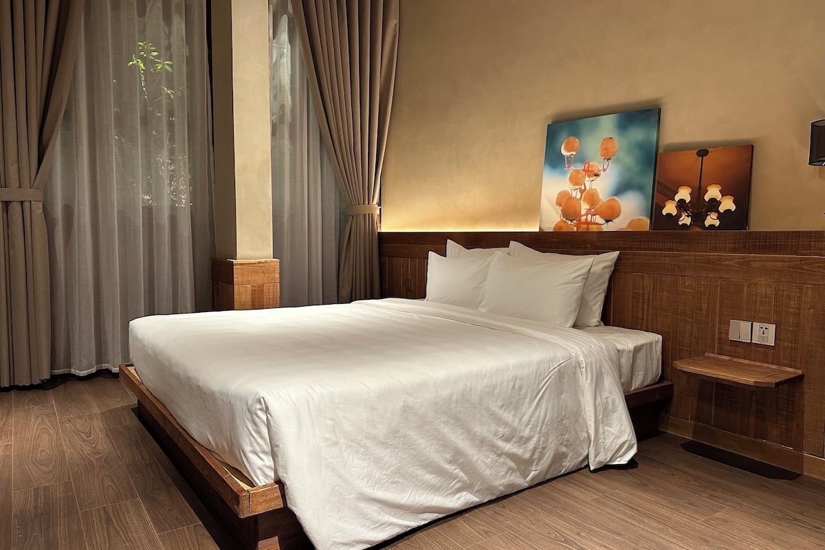 Une chambre d’hôtel avec un grand lit, une tête de lit en bois, une table de chevet et un tableau au mur.