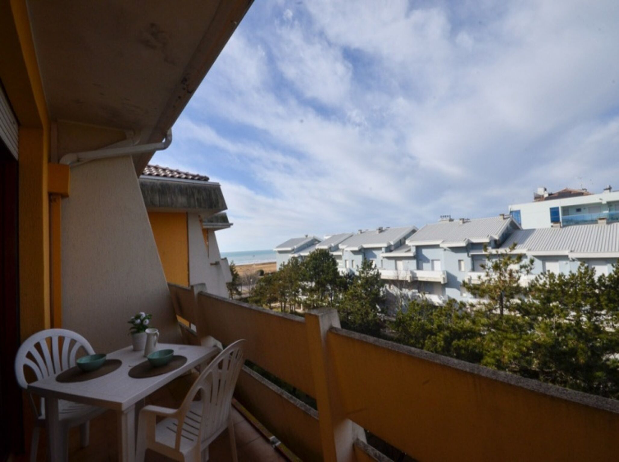 Ein Balkon mit Tisch und Stühlen, mit Blick auf eine Reihe moderner Gebäude und einen Strand.