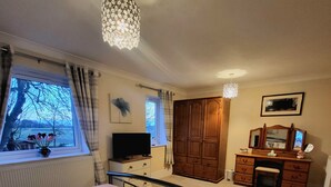 A bedroom with a bed, a dresser, a TV, a window with curtains, and a chandelier. - Three Farthings Bed & Breakfast, a quiet and peaceful countryside location. (Driffield)